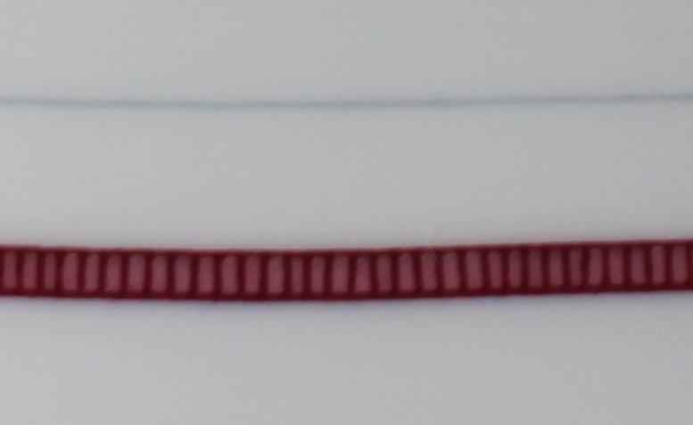 Detailansicht des Aragon Musters am Teller: breite rote Linie, hellrote Quadrate mit dunkelroten Trennstrichen, außen an beiden Seiten eine dunkelrote Linie. Dazu eine schmale grau / blaue Linie oberhalb der roten.